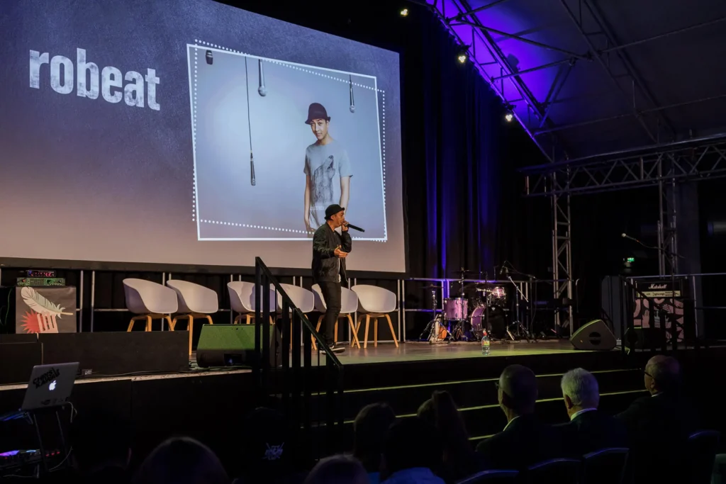 Robeat mit Mikrofon auf der Bühne vor einer großen Leinwand